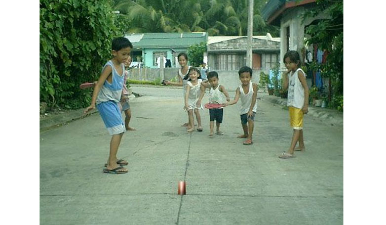 A group of children trying to knock the can from a circle on the ground using slippers